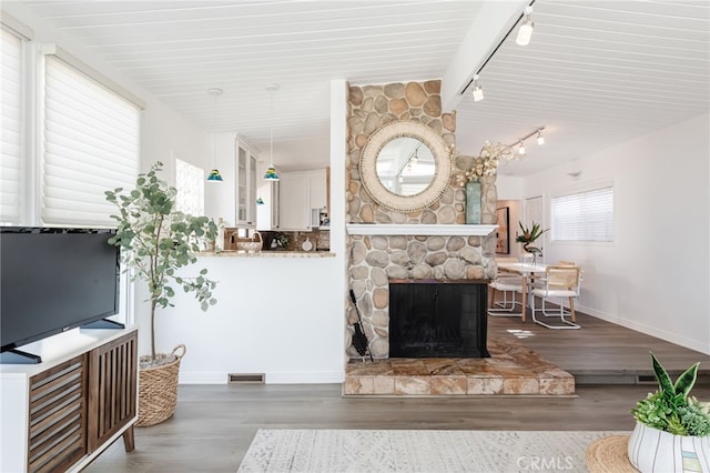 living room featuring wood finished floors, visible vents, baseboards, a fireplace, and rail lighting