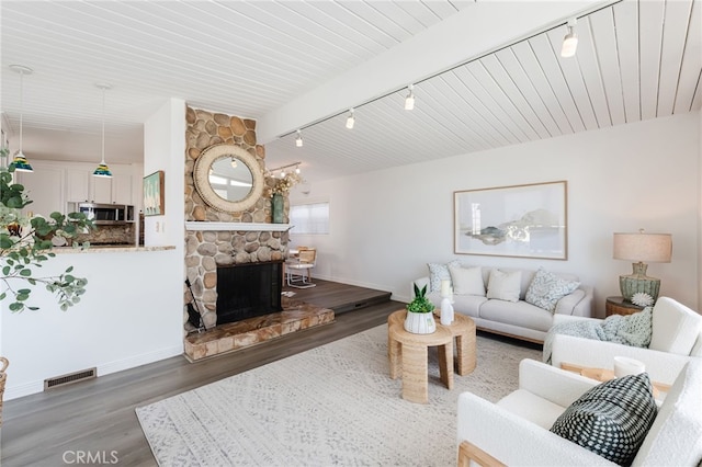 living room featuring wood finished floors, visible vents, baseboards, a fireplace, and rail lighting