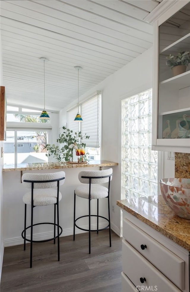 kitchen with light stone counters, a breakfast bar, dark wood-style floors, and white cabinetry