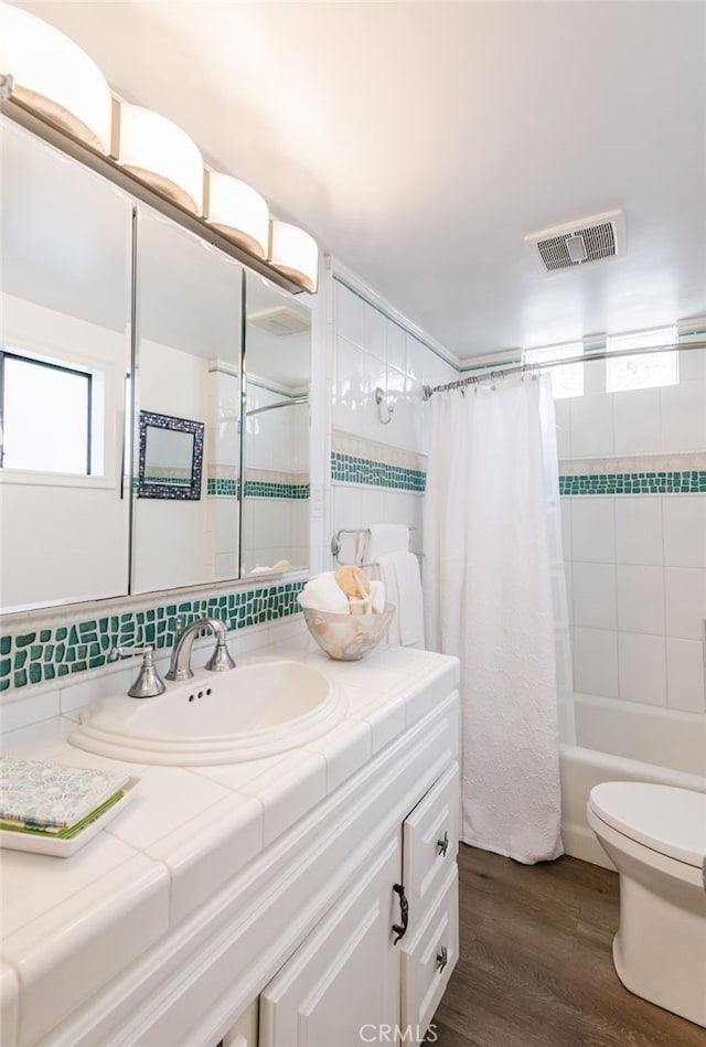 bathroom featuring visible vents, toilet, wood finished floors, vanity, and shower / bathtub combination with curtain