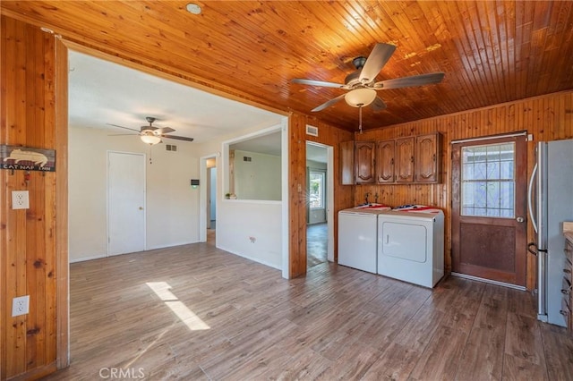 laundry area with cabinet space, wood ceiling, wood walls, separate washer and dryer, and wood finished floors