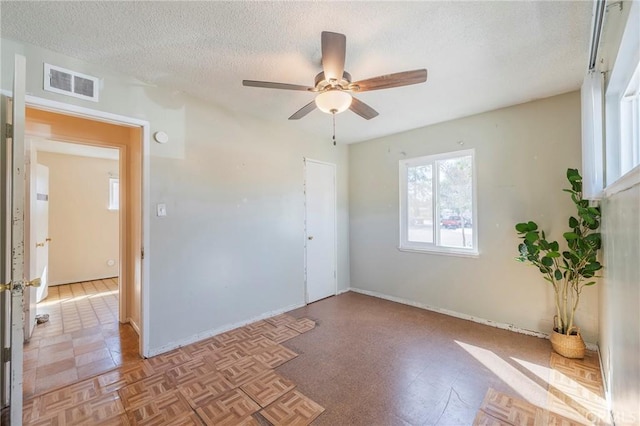 empty room featuring a ceiling fan, baseboards, visible vents, and a textured ceiling