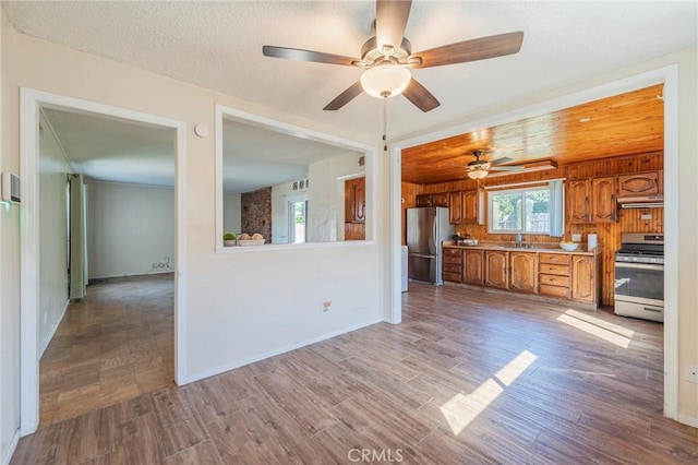 kitchen featuring brown cabinetry, appliances with stainless steel finishes, wood finished floors, light countertops, and a sink