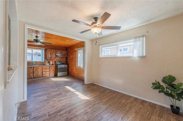 kitchen featuring stainless steel gas stove, brown cabinets, wood finished floors, a textured ceiling, and under cabinet range hood