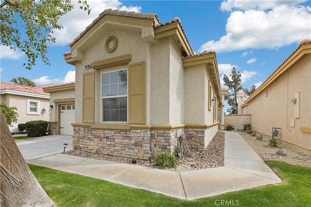 exterior space featuring stone siding, driveway, a tiled roof, and stucco siding