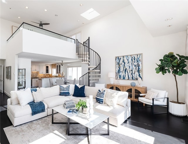 living room featuring ceiling fan, a high ceiling, wood finished floors, and stairs