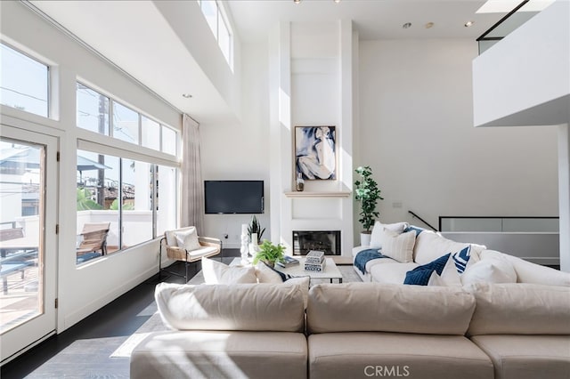 living room with dark wood-type flooring, a high ceiling, and a glass covered fireplace