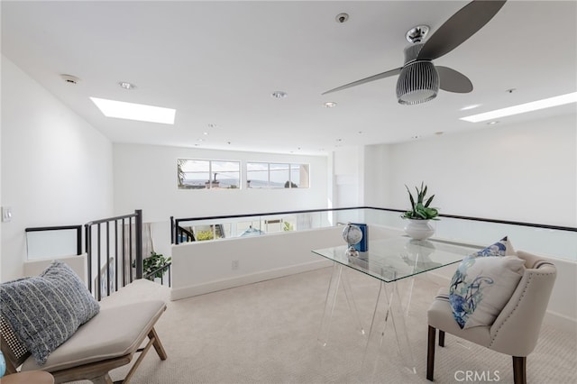 living area featuring a skylight, carpet flooring, baseboards, and ceiling fan