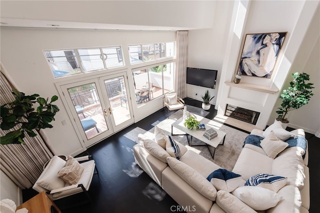 living area featuring plenty of natural light, french doors, baseboards, and a glass covered fireplace