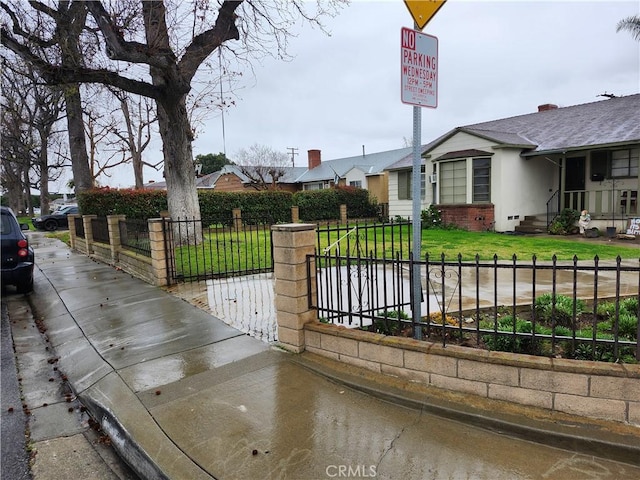 view of gate featuring a fenced front yard, a residential view, and a lawn