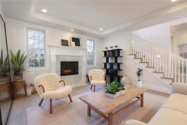 living area featuring light wood-style flooring, baseboards, stairs, a tiled fireplace, and crown molding