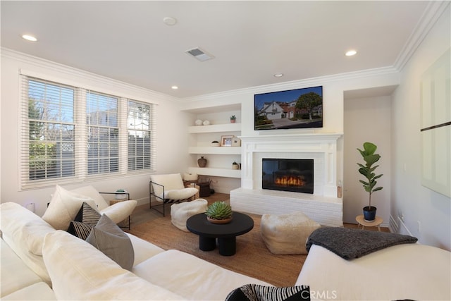 living room featuring a brick fireplace, built in shelves, visible vents, and ornamental molding