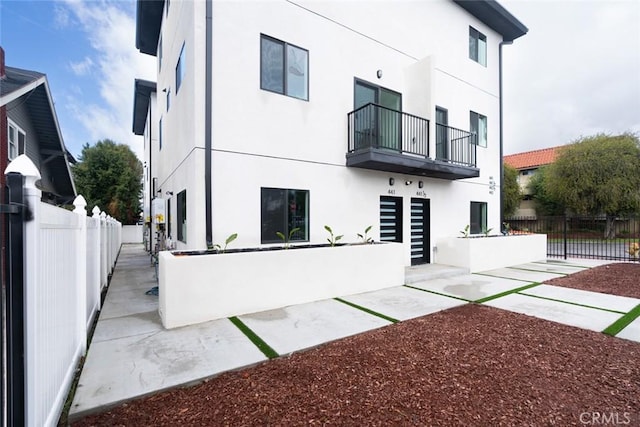 back of house featuring fence private yard, a balcony, and stucco siding