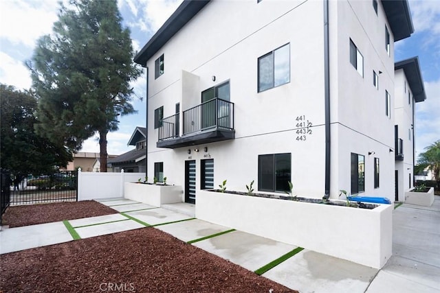 view of side of home with a balcony, a patio area, fence, and stucco siding