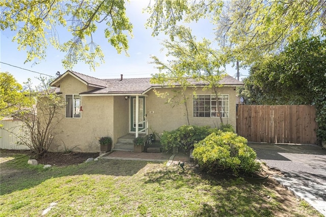 ranch-style house with roof with shingles, fence, a front lawn, and stucco siding