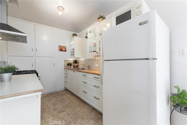 kitchen featuring a sink, white cabinets, wall chimney range hood, freestanding refrigerator, and decorative backsplash