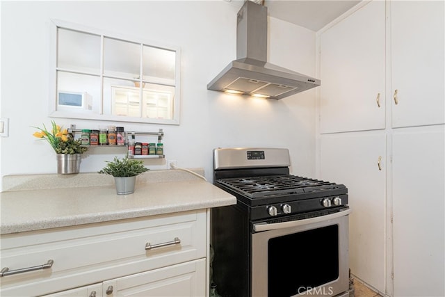 kitchen featuring light countertops, wall chimney range hood, gas stove, and white cabinetry