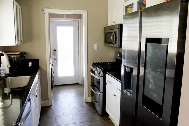 kitchen featuring dark tile patterned flooring, a sink, dark countertops, white cabinetry, and appliances with stainless steel finishes