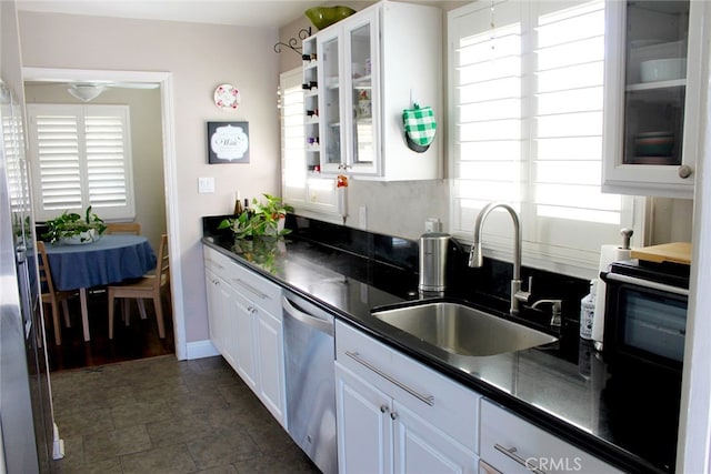 kitchen with dark countertops, a sink, white cabinets, and stainless steel dishwasher