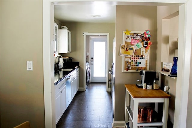 kitchen featuring a sink, baseboards, washer / dryer, white cabinets, and stainless steel dishwasher