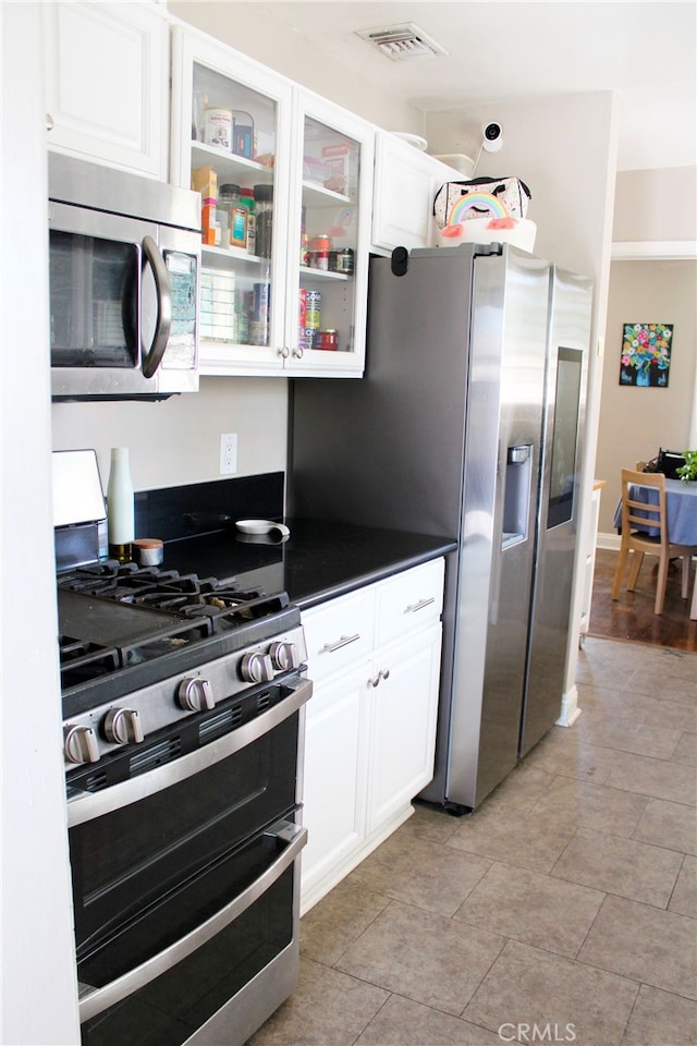 kitchen featuring visible vents, white cabinets, glass insert cabinets, appliances with stainless steel finishes, and dark countertops