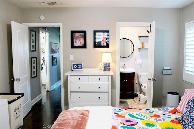 bedroom featuring visible vents, a sink, ensuite bathroom, and wood finished floors