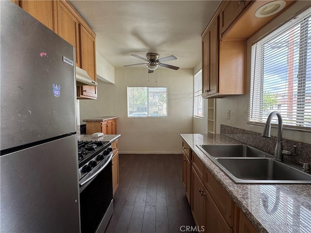 kitchen with dark wood-type flooring, under cabinet range hood, brown cabinets, appliances with stainless steel finishes, and a sink