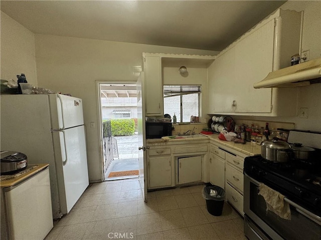 kitchen with stainless steel gas range oven, tile counters, freestanding refrigerator, white cabinets, and a sink