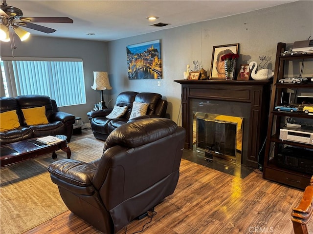 living area with ceiling fan, visible vents, wood finished floors, and a tile fireplace