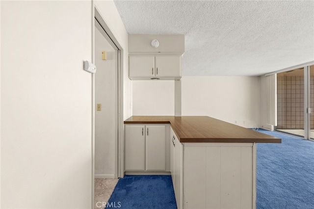 kitchen featuring a peninsula, butcher block countertops, white cabinets, a textured ceiling, and light colored carpet