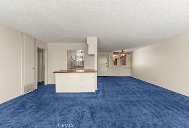 unfurnished living room featuring a ceiling fan, visible vents, dark carpet, and a textured ceiling