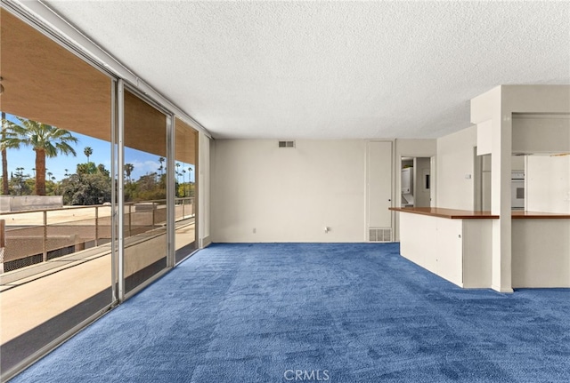 unfurnished living room with a wall of windows, visible vents, a textured ceiling, and carpet flooring