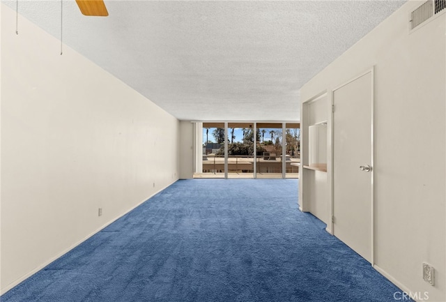 carpeted empty room featuring ceiling fan, expansive windows, visible vents, and a textured ceiling