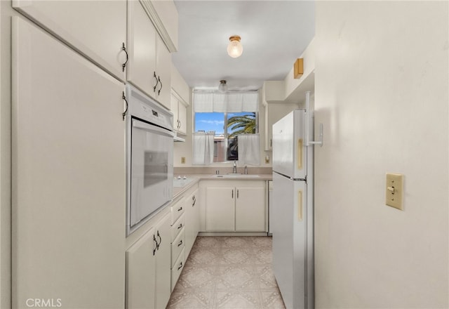 kitchen featuring a sink, white cabinetry, white appliances, light countertops, and light floors