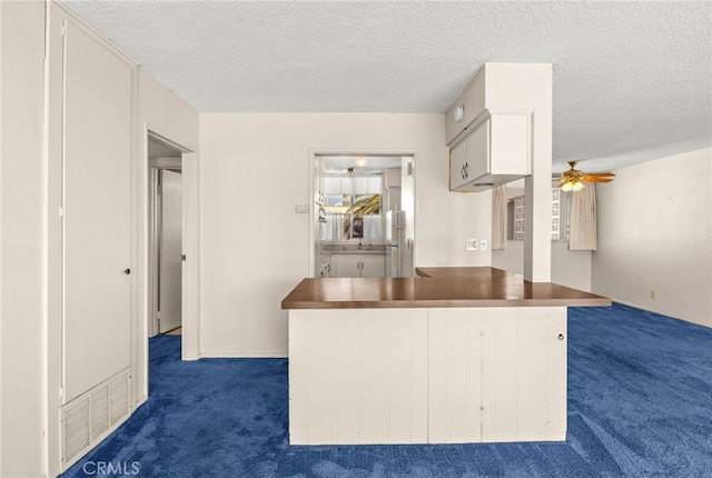 kitchen with a textured ceiling, dark carpet, white cabinetry, a peninsula, and ceiling fan