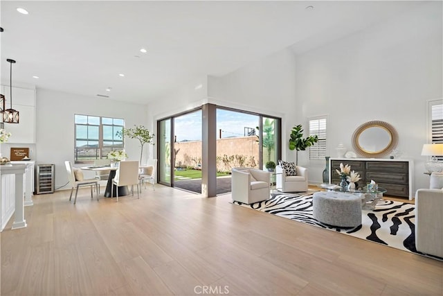 living area featuring wine cooler, recessed lighting, light wood-style flooring, and a towering ceiling