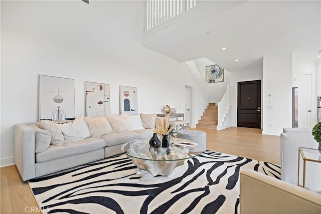 living room featuring light wood-type flooring, baseboards, a high ceiling, and stairs