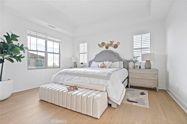 bedroom with a raised ceiling, wood finished floors, visible vents, and baseboards