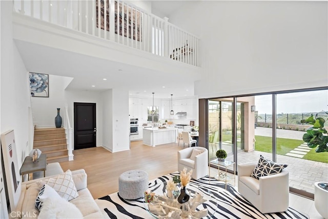 living room featuring light wood finished floors, stairway, recessed lighting, and a high ceiling