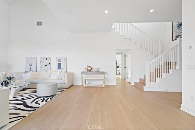 living room with visible vents, wood finished floors, a towering ceiling, and stairs