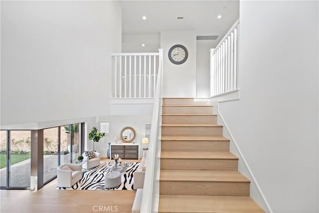 stairs with recessed lighting, a high ceiling, baseboards, and wood finished floors