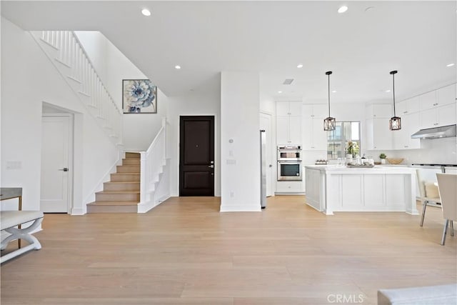 kitchen with under cabinet range hood, white cabinetry, light wood-style floors, double oven, and light countertops