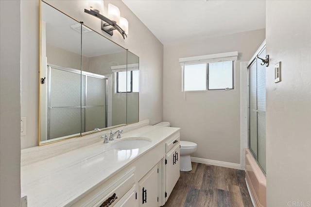 bathroom featuring shower / bath combination with glass door, toilet, vanity, wood finished floors, and baseboards