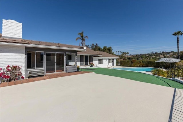 rear view of house featuring brick siding, a chimney, an outdoor pool, and a patio