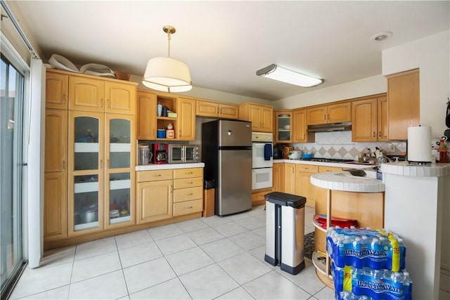 kitchen featuring backsplash, double oven, freestanding refrigerator, glass insert cabinets, and under cabinet range hood