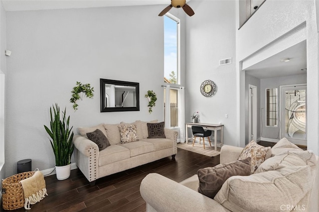 living area with baseboards, visible vents, a ceiling fan, a towering ceiling, and wood finish floors