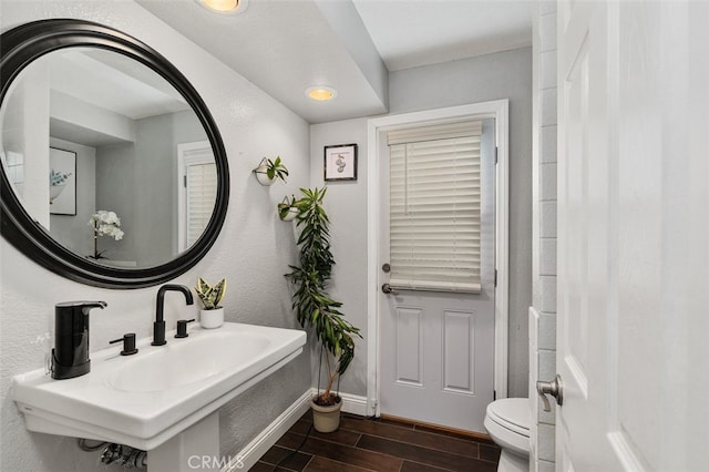 bathroom featuring baseboards, a textured wall, toilet, wood finish floors, and a sink