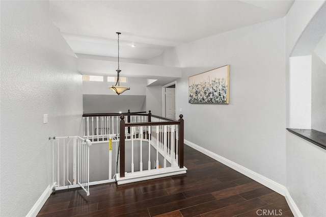 hallway featuring baseboards, wood finished floors, and an upstairs landing