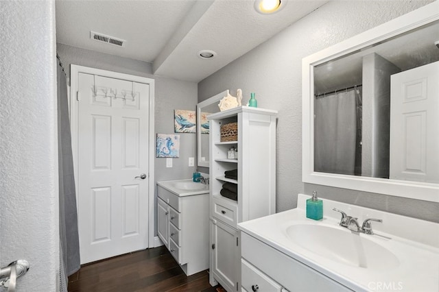 full bathroom featuring a textured wall, vanity, wood finished floors, and visible vents