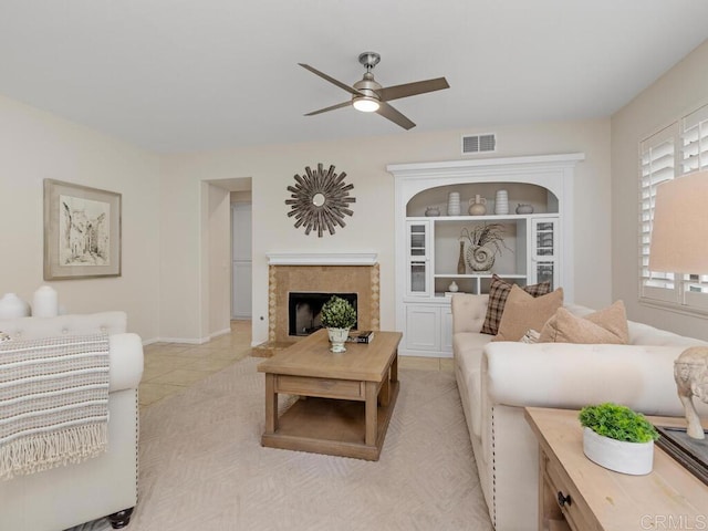 living room featuring light tile patterned floors, a premium fireplace, visible vents, and a ceiling fan